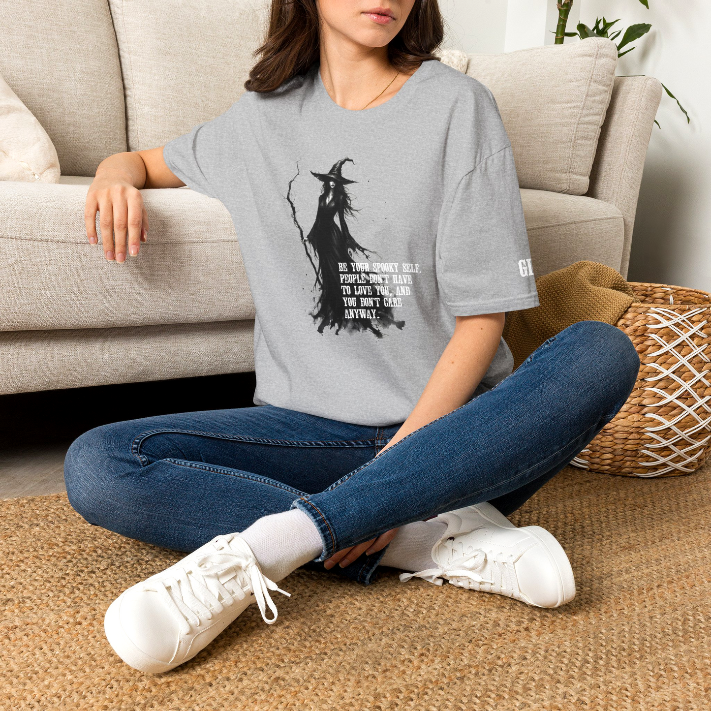 Young college girl wearing a gothic witch graphic t-shirt featuring a detailed illustration of a witch holding a staff, surrounded by the quote 'Be your spooky self. People don't have to love you, and you don't care anyway.' Designed and sold in The Fright Factory NOLA gothic gift shop.