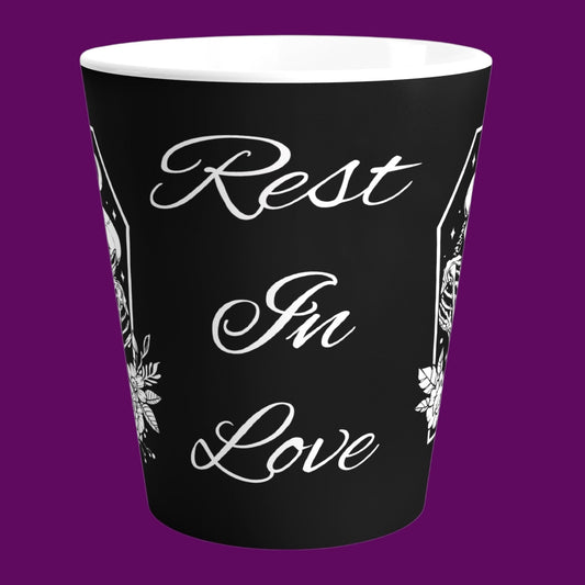 A custom matte black ceramic latte mug with a white interior, featuring two skeletons in embrace with the phrase "Rest In Love" written in elegant white cursive script down the center. Personalize in The Fright Factory New Orleans.