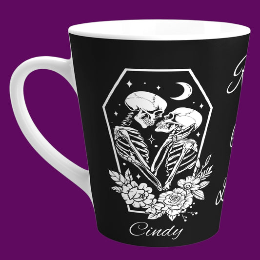 A custom matte black ceramic coffee mug with a white interior, featuring two skeletons in embrace with the phrase "Rest In Love" written in elegant white cursive script down the center. Personalize in The Fright Factory New Orleans.