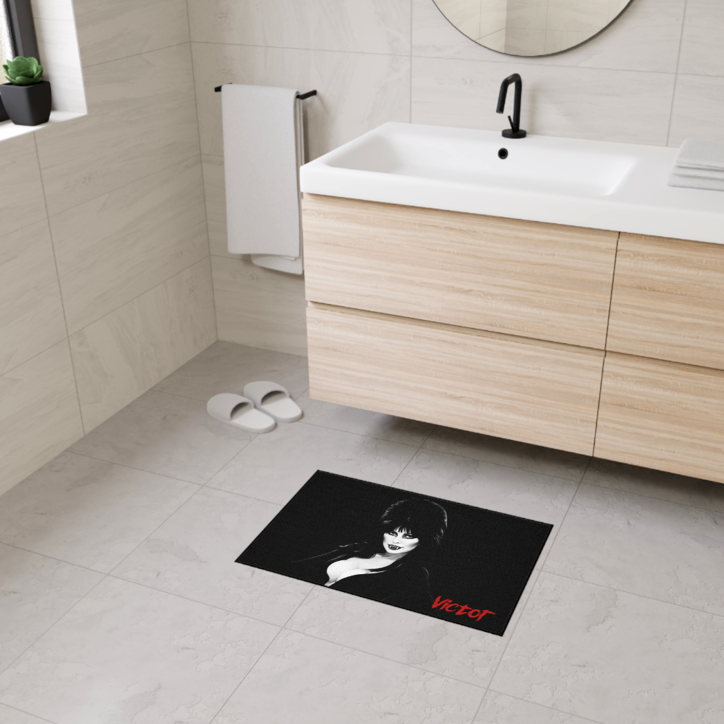 A horror-themed Elvira bath mat placed on a tiled bathroom floor in front of a white bathtub, adding a gothic aesthetic to the room.