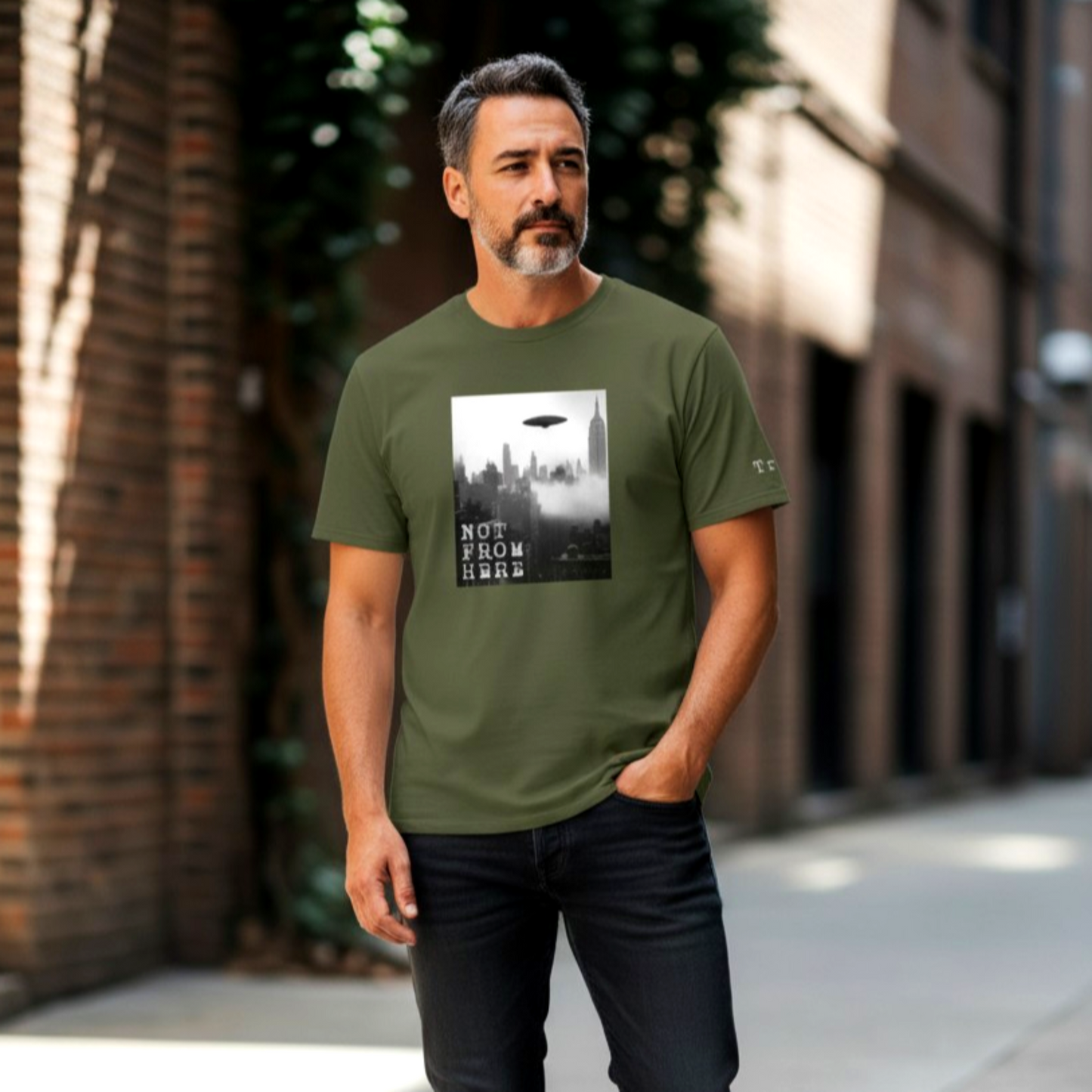 Model wearing a olive green graphic t-shirt featuring a vintage black and white UFO sighting over a foggy New York City skyline. For ale in The Fright Factory New Orleans.